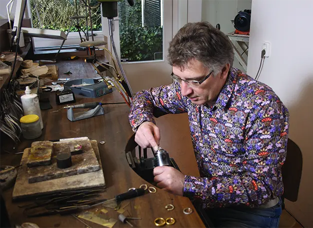 Guus aan de goudsmidswerkbank, met ringen en gereedschap voor zich